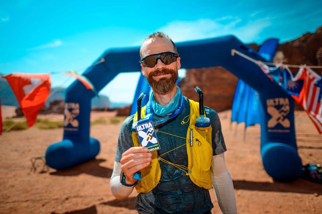 Brendan Ellis holding his Ultra X Jordan finisher medal in the desert
